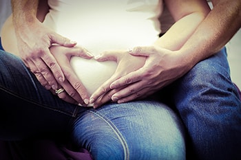 Couple making heart on pregnant mom's tummy