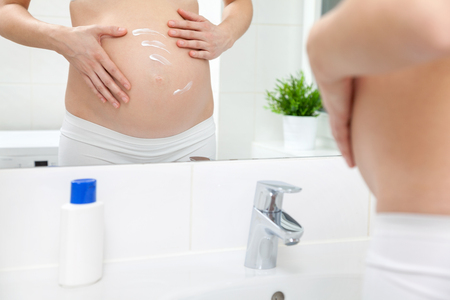 Pregnant woman applying lotion
